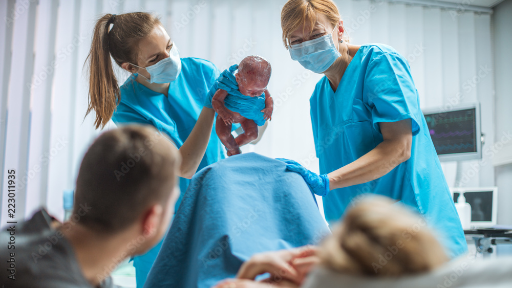 在医院助产士抱着婴儿。分娩中的妇女推着婴儿分娩，产科医生如是说