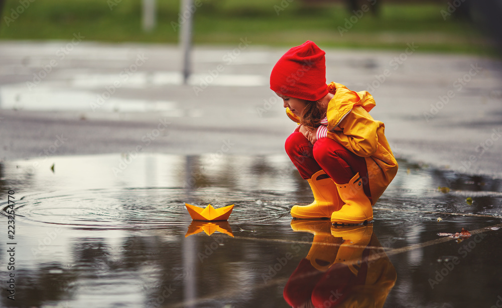 快乐的小女孩，带着雨伞和纸船，在秋天的水坑里享受大自然。