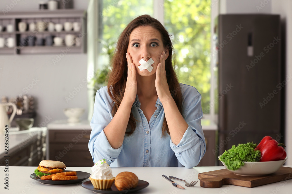 嘴上粘着胶带、厨房里有不同产品的压力大的女人。在健康和不健康之间做出选择