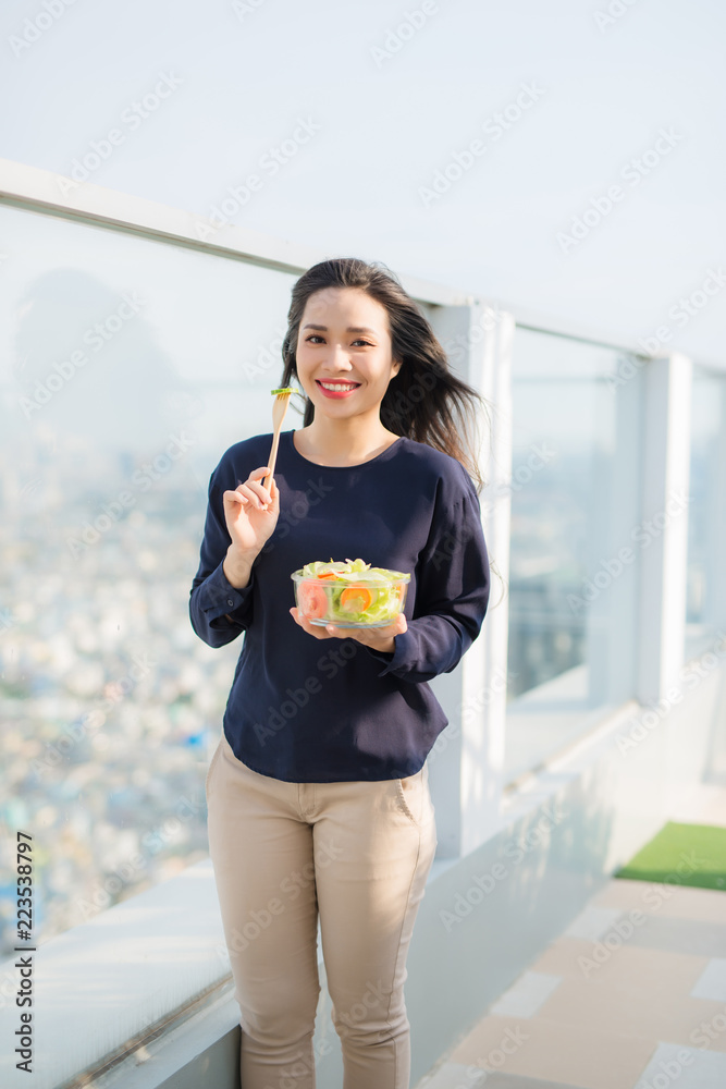 一个阳光明媚的夏日，一个迷人的高加索微笑女人坐在绿色的g上吃沙拉的画像