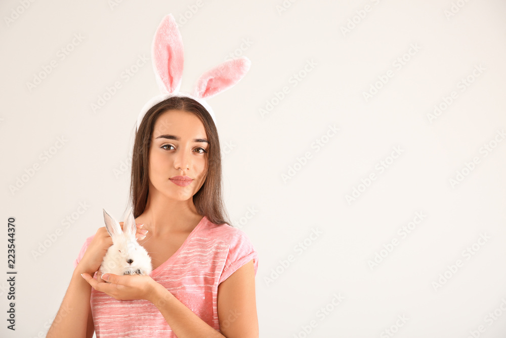 美丽的年轻女人，兔子耳朵和可爱的兔子在浅色背景下