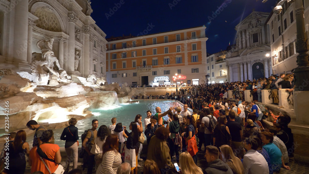 人们在晚上为美丽的Fontana di Trevi拍照。