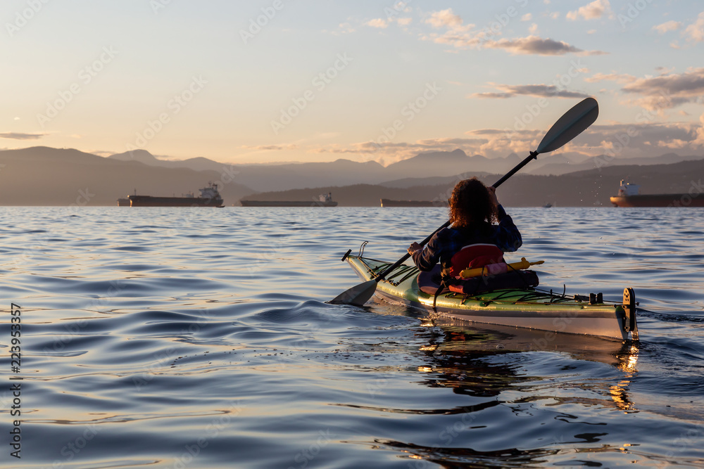 在充满活力的阳光明媚的夏季日落中，女孩海上皮划艇。拍摄于加拿大不列颠哥伦比亚省温哥华市。