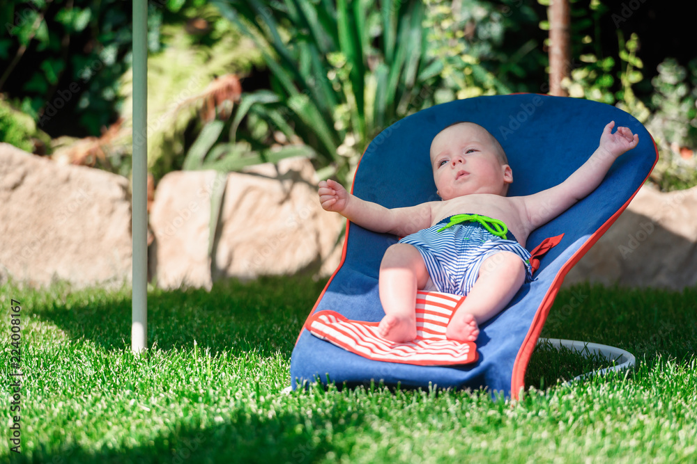 男婴躺在绿色草坪上的躺椅上。放松和度假的概念