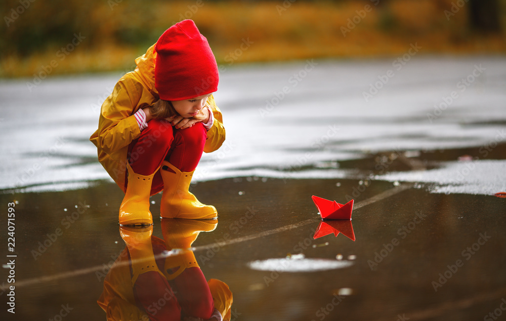 秋天在水坑里玩纸船的快乐女孩