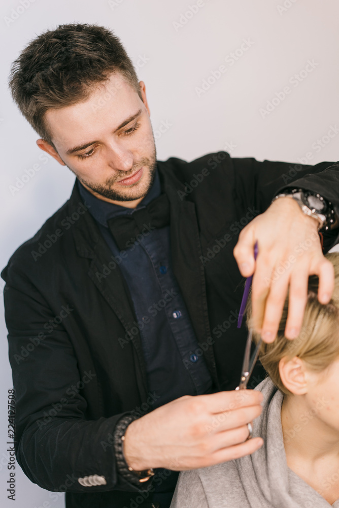 穿着时尚服装的理发师在理发机中使用梳子和剪刀为客户制作发型