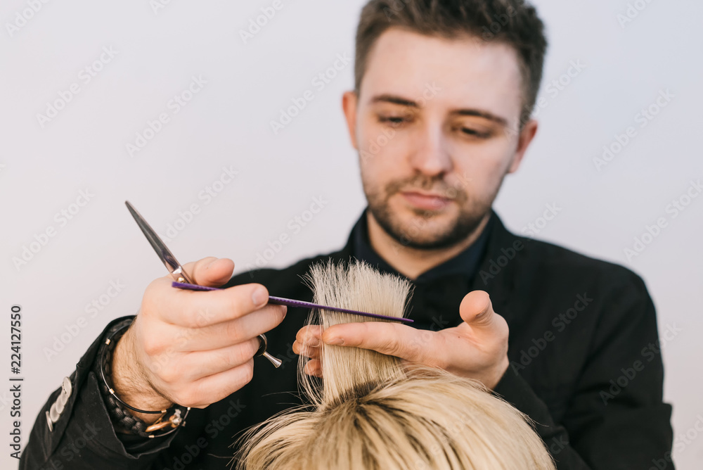 年轻的理发师在美容室里为一位女士剪下一缕白发。特写