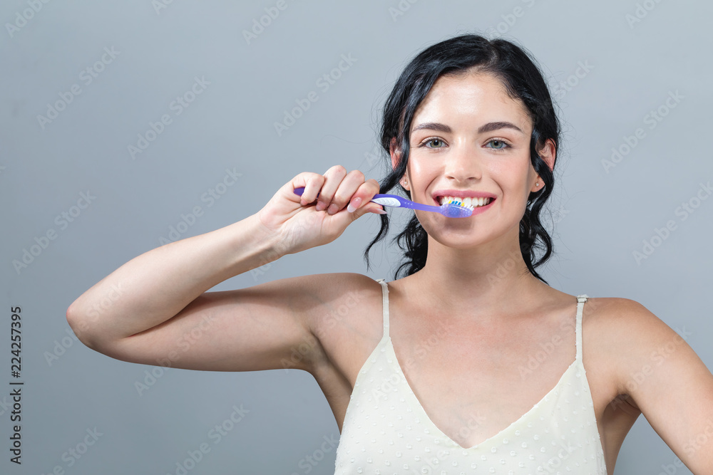 灰色背景下拿着牙刷的年轻女性