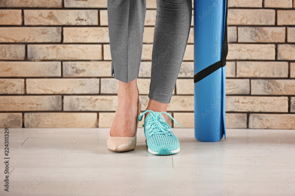 在砖墙附近穿着高跟鞋和运动鞋的年轻女性。休息和运动之间的平衡概念