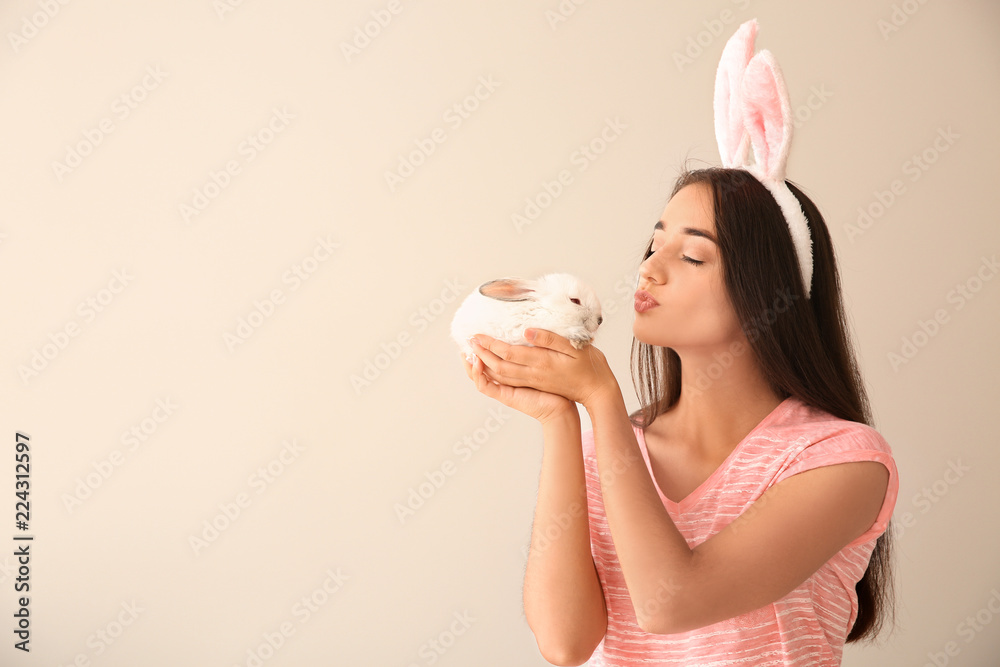 美丽的年轻女人，兔子耳朵和可爱的兔子在浅色背景下