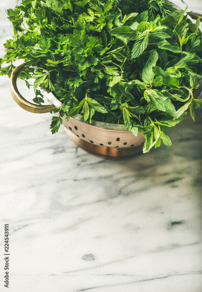 大理石厨房桌子上方的黄铜漏勺中的一束新鲜绿色花园草本植物，俯视图，复制空间