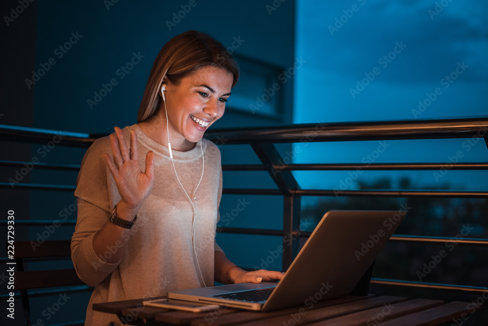 Young smiling woman having a video call using laptop, at night.