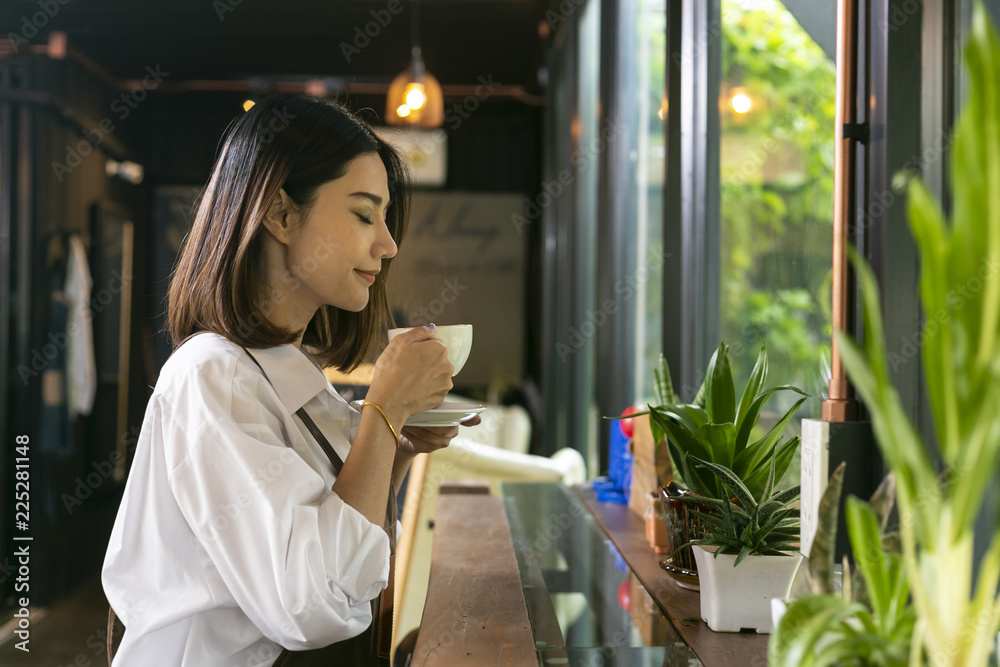 亚洲女人闻着咖啡，喝着热咖啡，在咖啡馆里感觉很好。