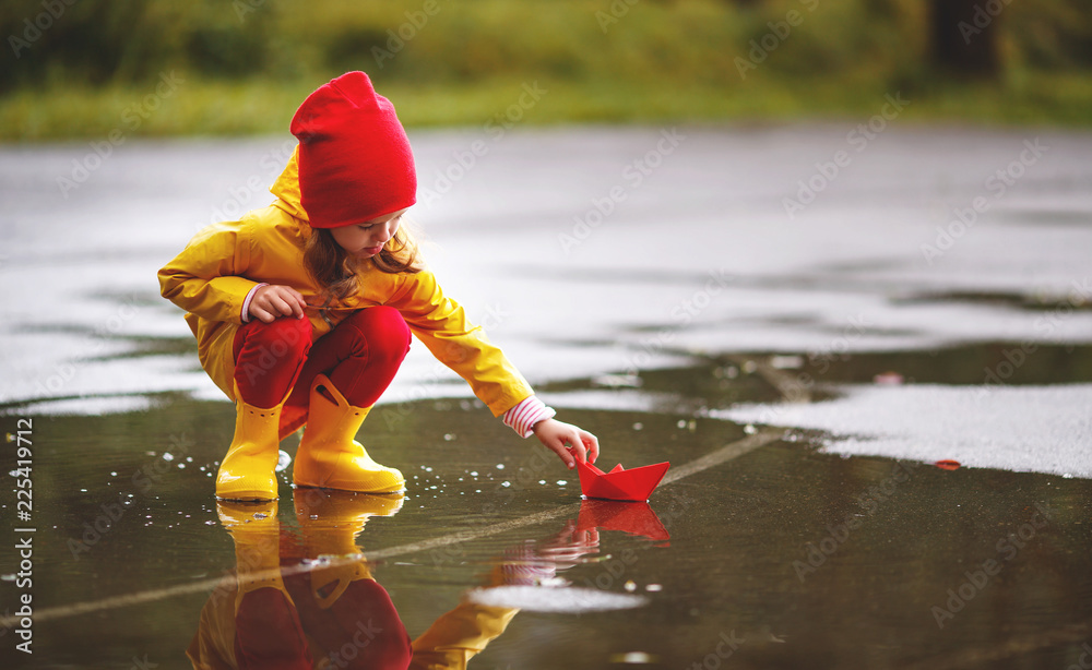 在大自然的秋天，在水坑里玩纸船的快乐小女孩