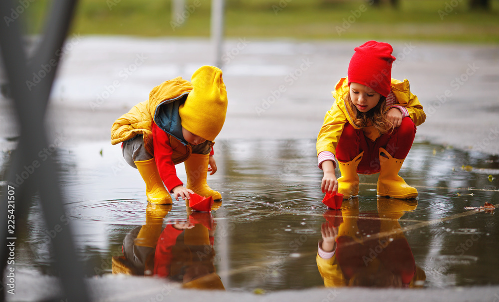 快乐的孩子女孩和男孩在秋天的水坑里用纸船在大自然上