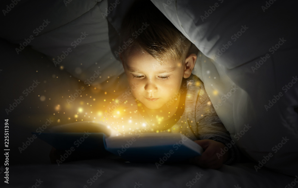 可爱的小男孩在床上盖着毯子看书