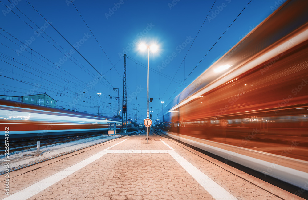 两列高速列车夜间在火车站上行驶。移动模糊的现代城际列车