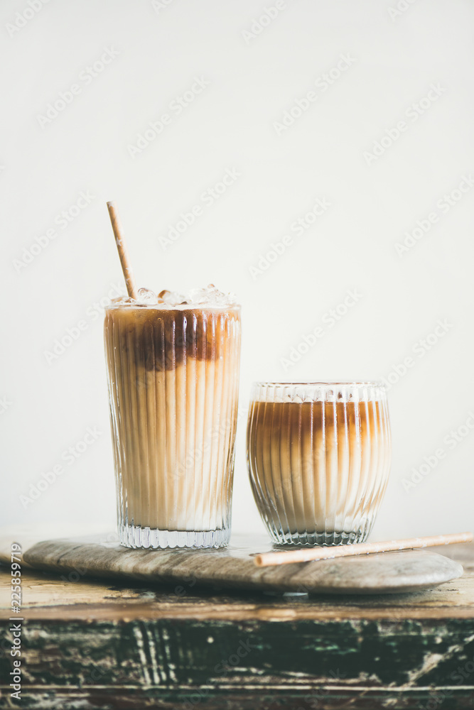 高玻璃杯中的冰咖啡，上面有牛奶和吸管，背景为白色墙壁，复制空间。总和