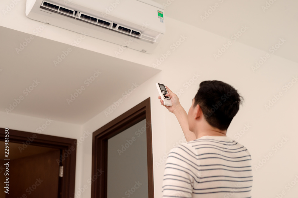 年轻人用遥控器打开或调整客厅壁挂式空调