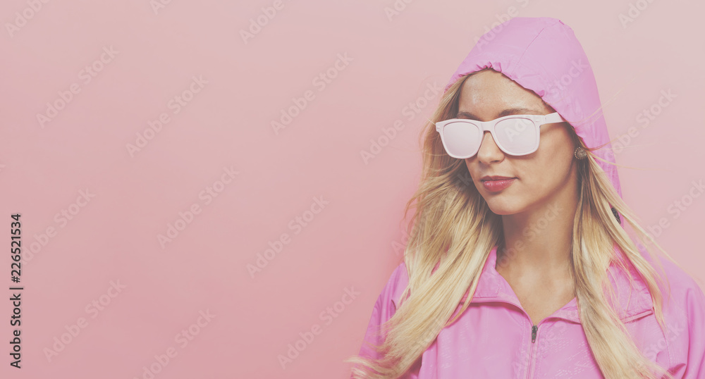 Fashionable woman in pink raincoat and sunglasses on a pink background