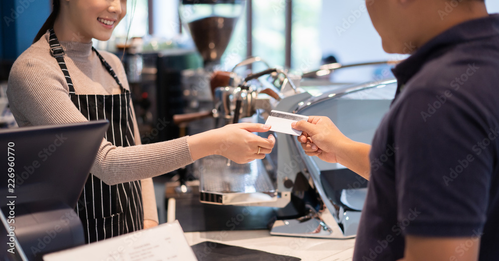 亚洲女咖啡师在咖啡店接受顾客的信用卡。