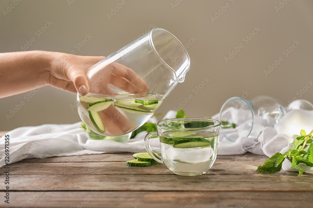 一个女人把美味的黄瓜水从罐子里倒进木桌上的杯子里