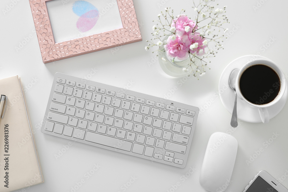 工作场所配有电脑键盘，白色桌子上摆放着一束美丽的粉红色花朵，俯视图