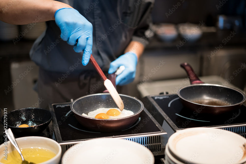 酒店厨师戴着手套在酒店餐厅的热锅上煮煎蛋，作为早餐。
