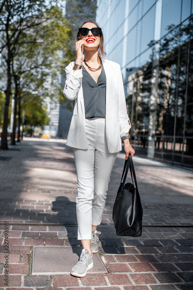 金融区一位身穿白色西装、手持智能手机的商务女性的生活方式画像