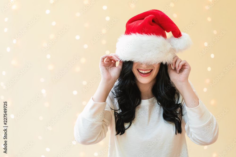 一个戴着圣诞老人帽子的女人在闪亮的灯光背景下遮住了眼睛