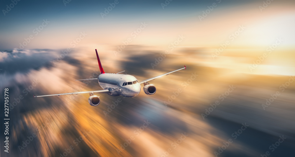 White airplane is flying in low clouds at sunset. Landscape with passenger airplane, blurred clouds,