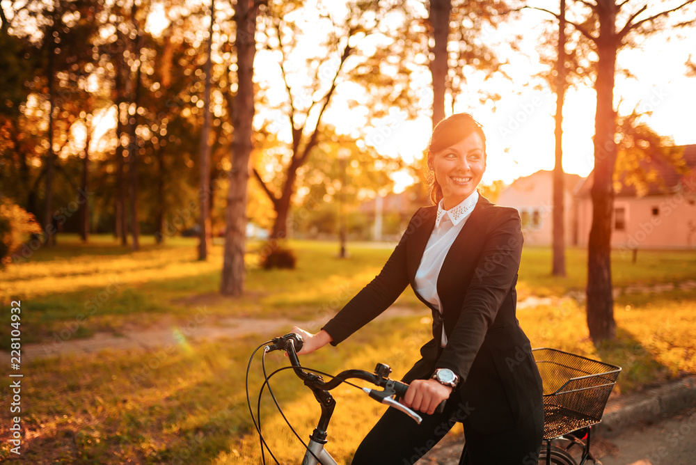 年轻的微笑女人下班后骑自行车穿过公园。