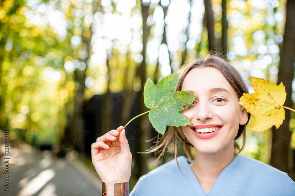 秋天在森林里，一位美丽的女子在户外用五颜六色的树叶近照