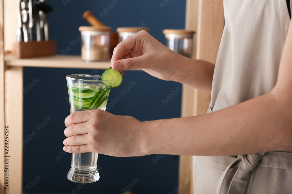 女人在室内拿着装有美味新鲜黄瓜水的玻璃杯