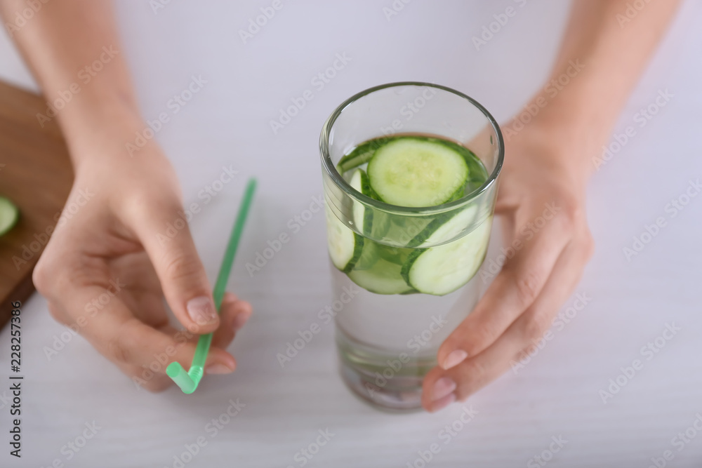 一个女人拿着一个杯子，杯子里放着美味的新鲜黄瓜水和吸管放在浅色桌子上
