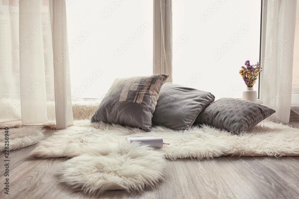 舒适的休息场所，窗户附近有柔软的枕头和毛茸茸的地毯