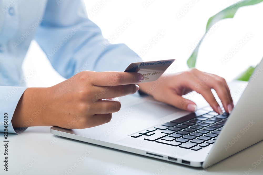 一个女人在笔记本电脑上打字并持有信用卡的特写