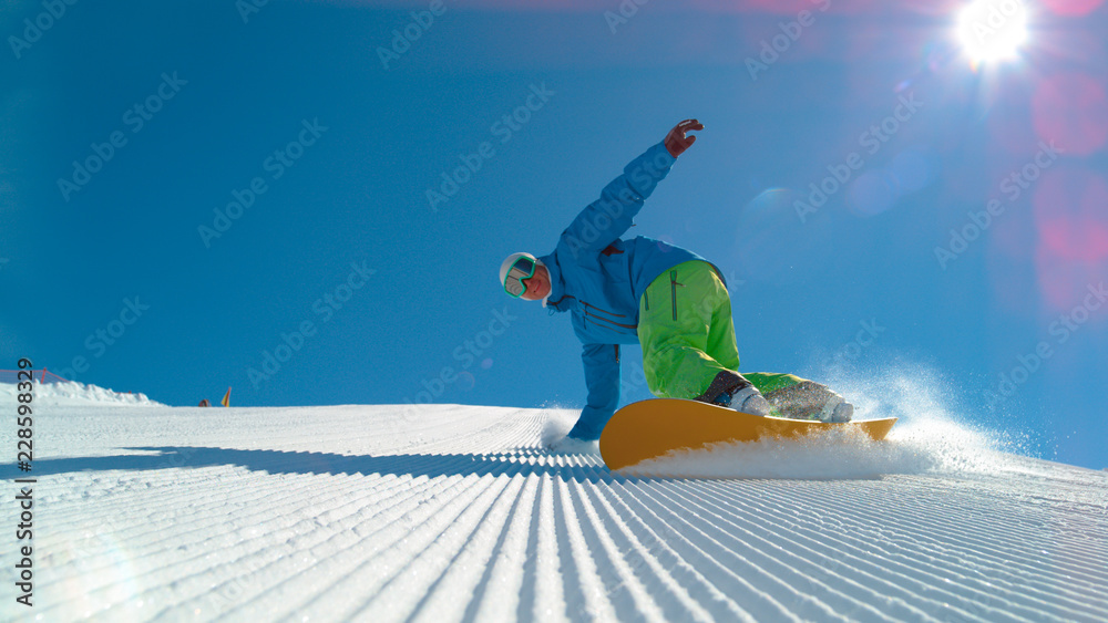 低角度：兴高采烈的年轻男性滑雪板运动员在一个新修整的斜坡上雕刻。