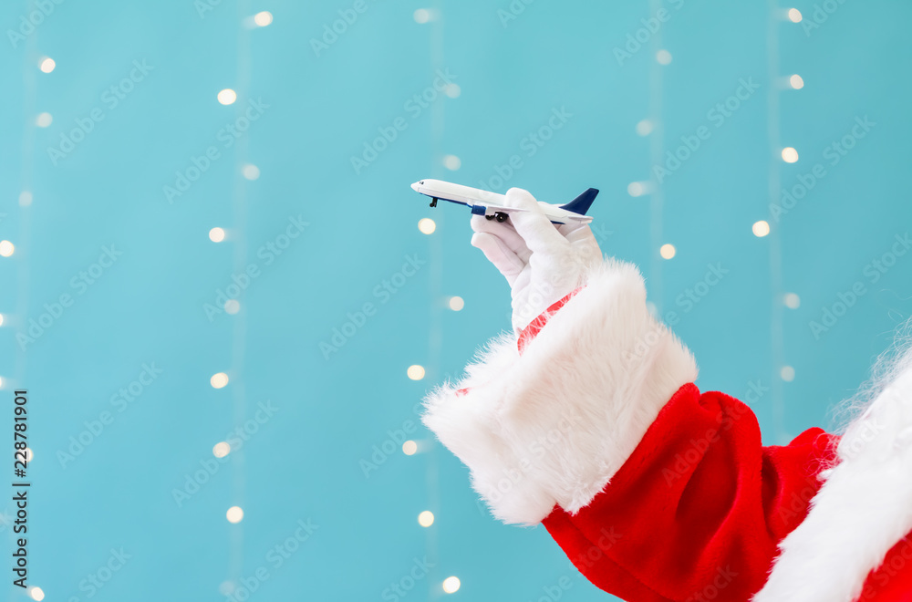 圣诞老人拿着一架玩具飞机，背景是闪亮的浅蓝色