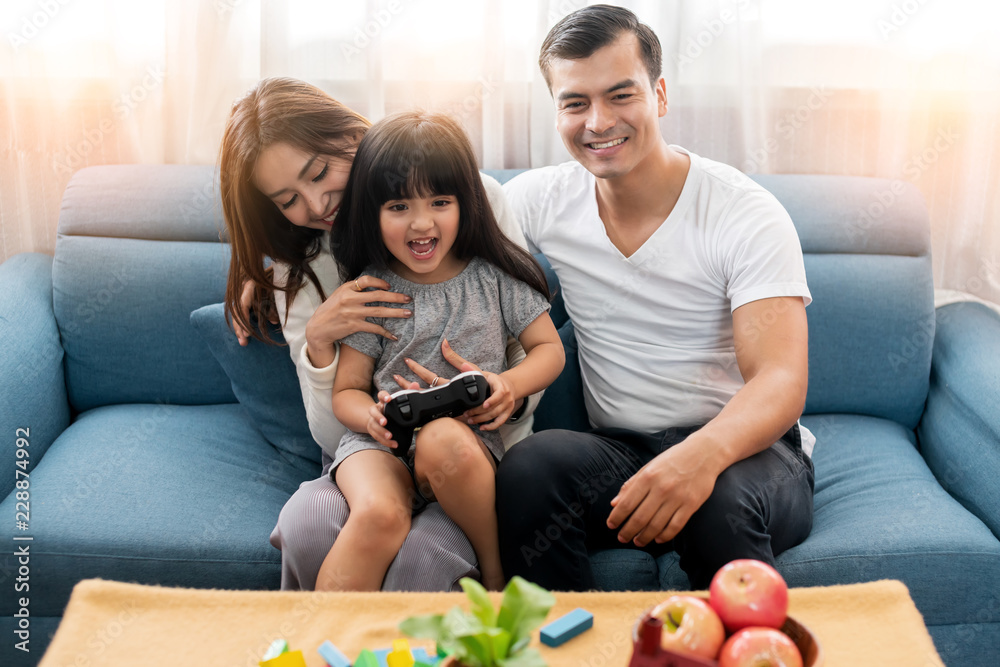 幸福家庭的父母看着女儿在客厅里一起玩电子游戏和欢笑