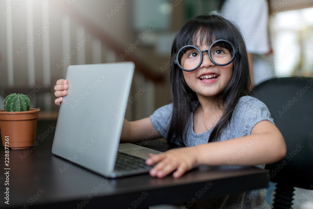 戴眼镜的可爱小女儿玩笔记本电脑玩得很开心，假装在家工作