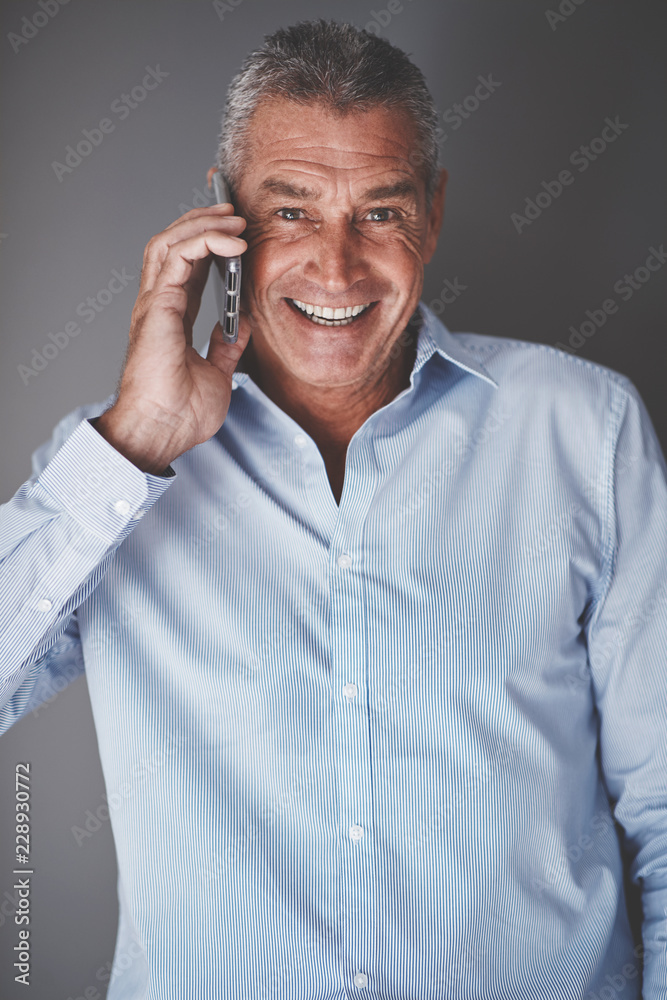 微笑的成熟商人用手机对着一个灰色的ba