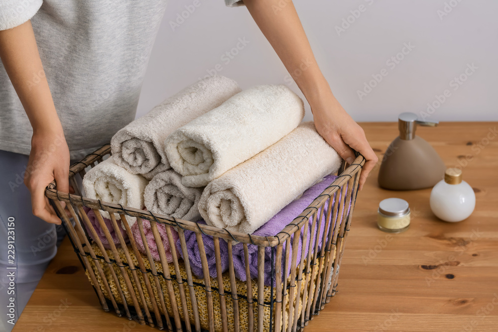 妇女在木桌旁将干净的软毛巾折叠到篮子里