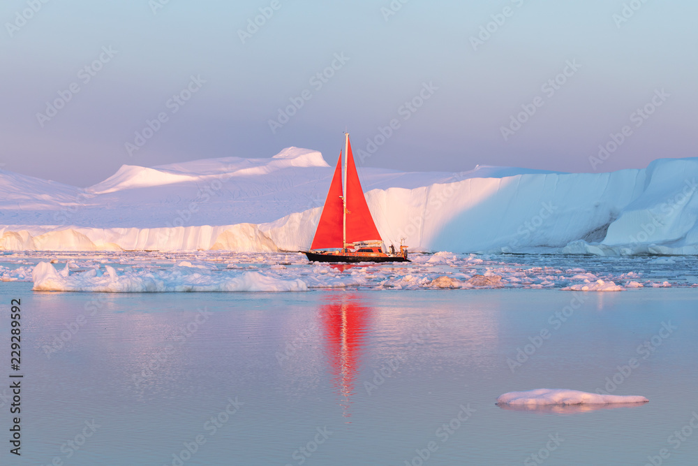 午夜阳光季节，一艘红色小帆船在迪斯科湾冰川的漂浮冰山中巡航