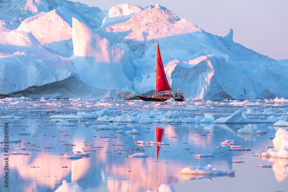 午夜阳光季节，一艘红色小帆船在迪斯科湾冰川的漂浮冰山中巡航