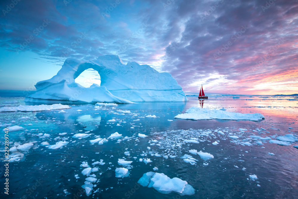 午夜阳光季节，红色小帆船在迪斯科湾冰川的漂浮冰山间巡航