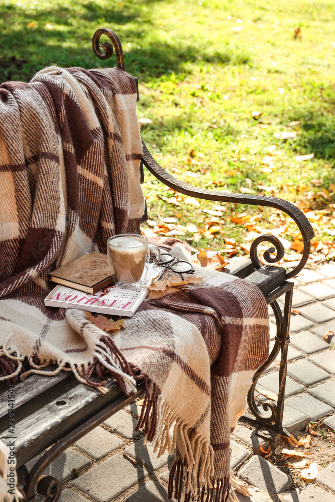 秋天公园木长椅上的一杯热咖啡，上面有温暖的格子、书籍和杂志