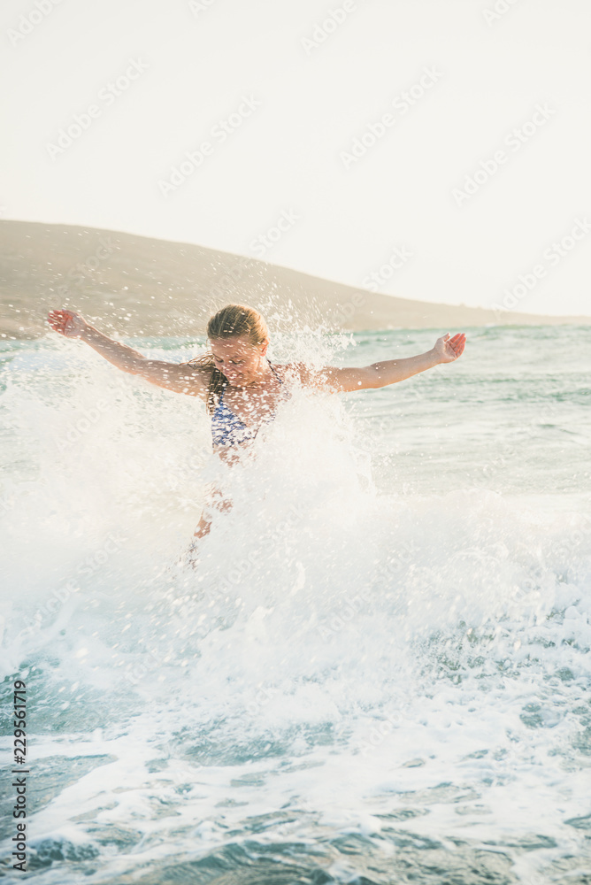 年轻漂亮的金发女子游客，穿着泳衣，站在那里享受Medit的波浪飞溅