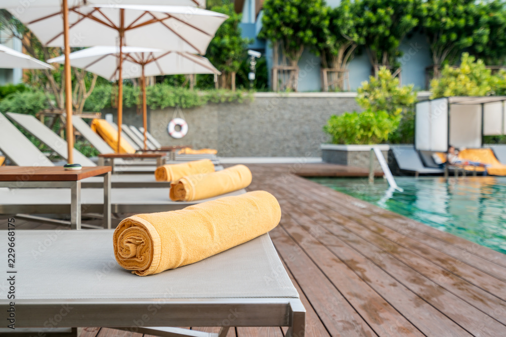 在度假村或酒店游泳池的日光躺椅背景上，卷起的橙色毛巾。