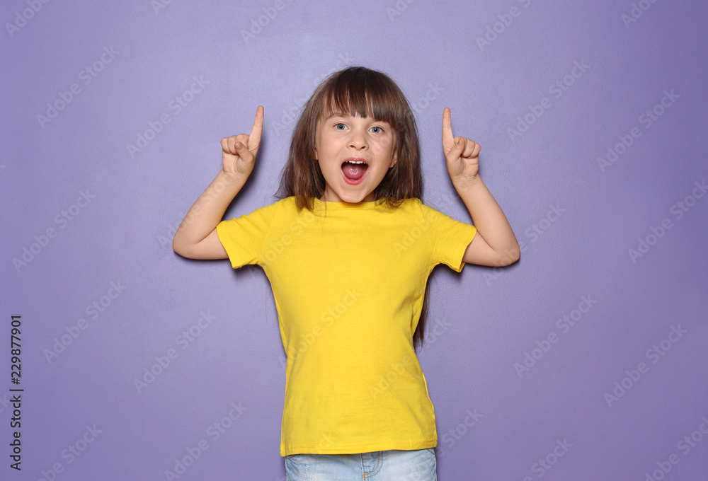 穿着t恤的小女孩指着彩色背景上的东西